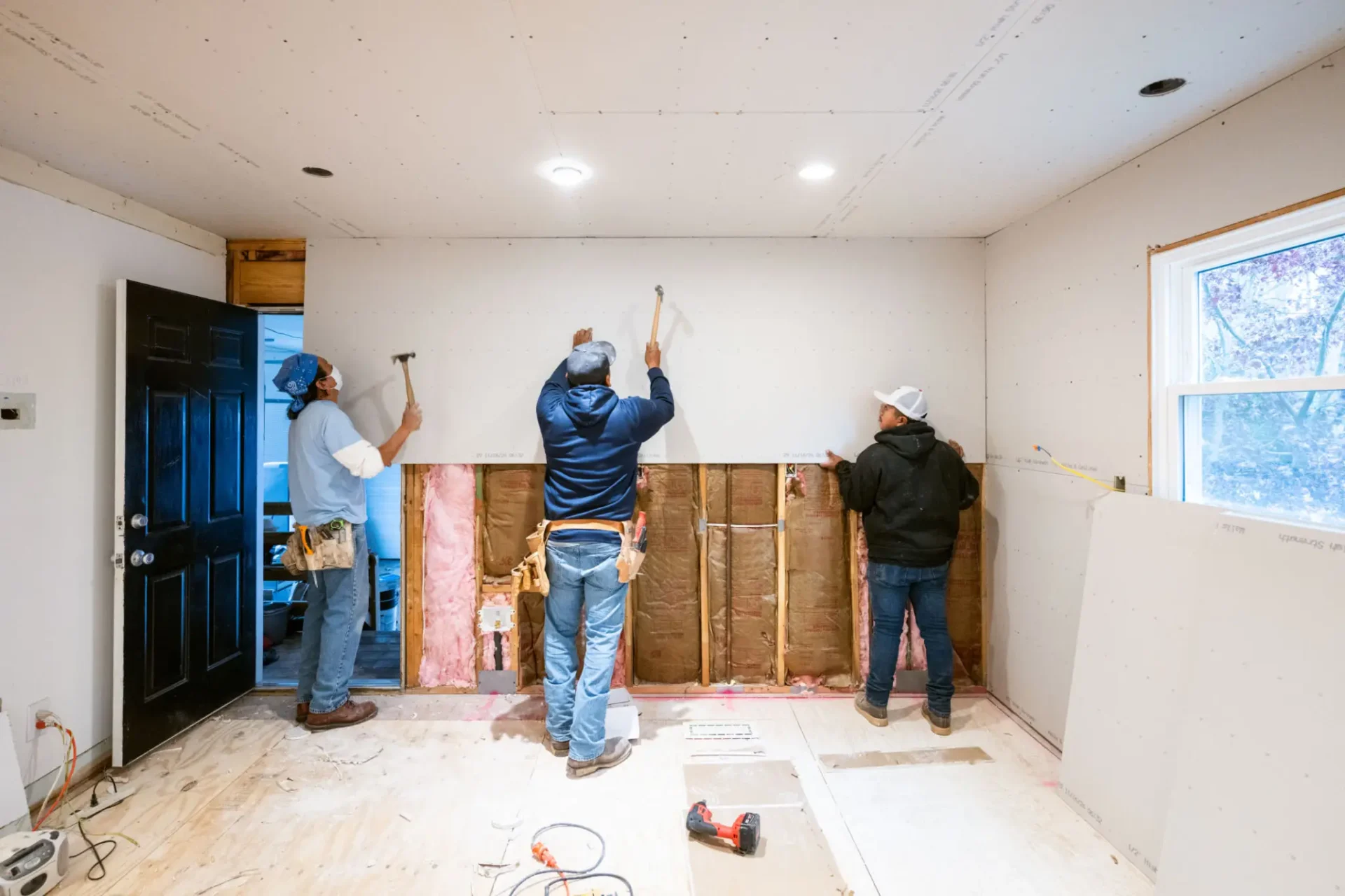 Three workers renovating a damaged wall in a room.