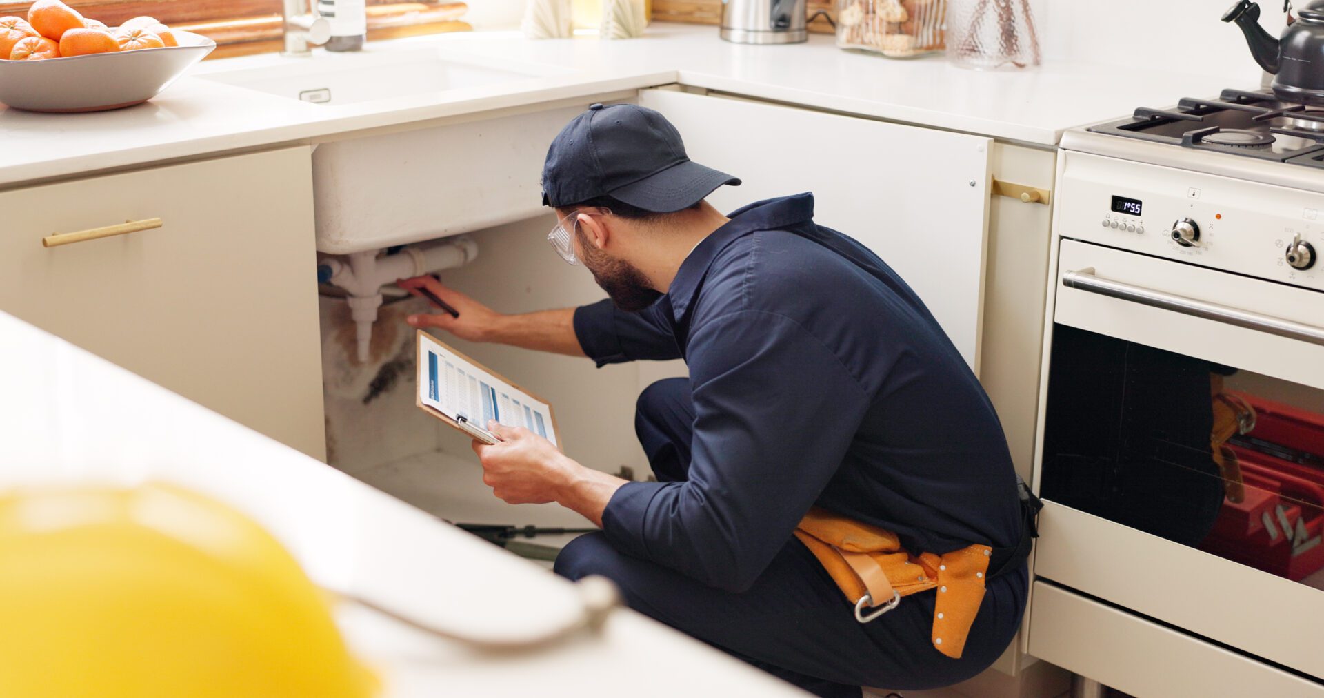 Technician inspecting plumbing under a kitchen sink using a tablet.