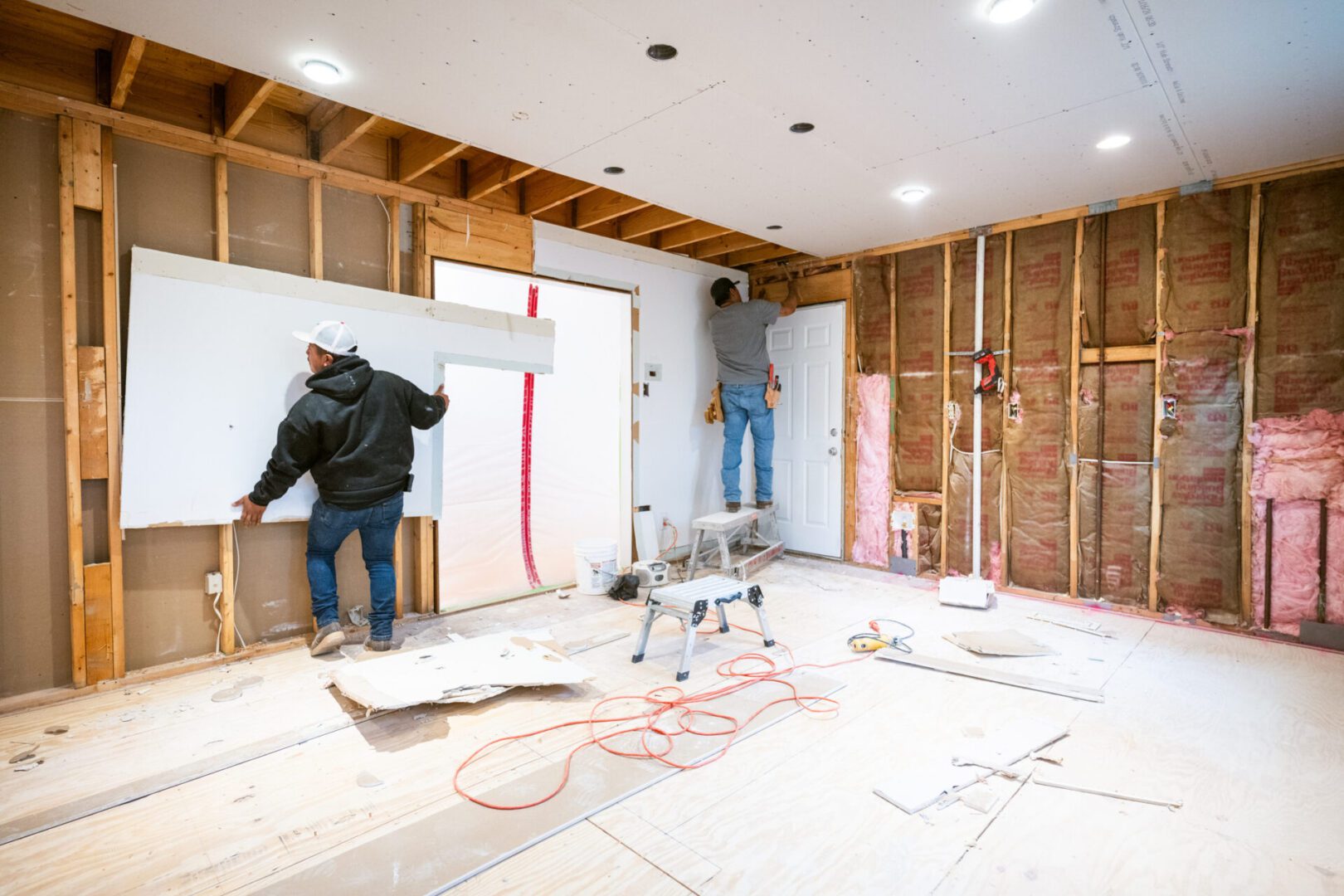 Two workers renovating a room with exposed walls and construction tools.