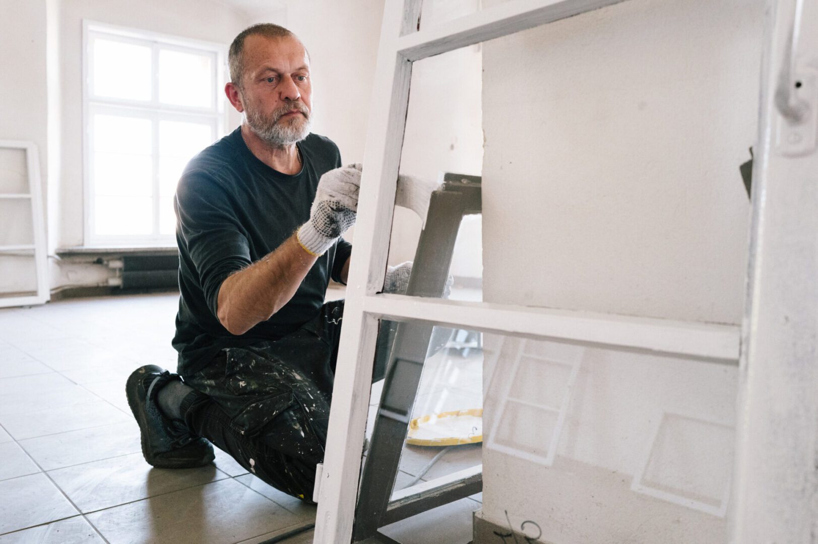 Man painting a white wooden ladder indoors.