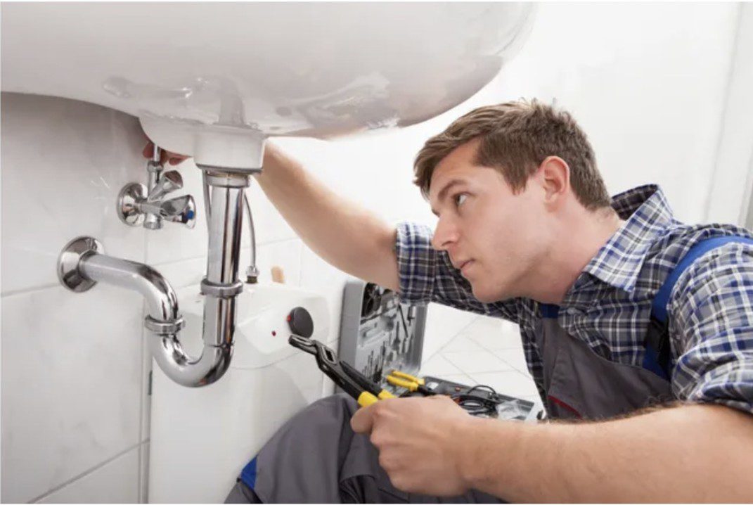 A plumber fixing pipes under a sink with tools.